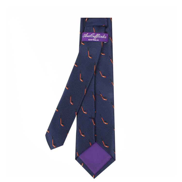 A dark blue tie with small red and orange pipe motifs, featuring a purple label that reads "Field Hockey Skinny Tie." The inner lining is purple, capturing an understated athletic spirit.