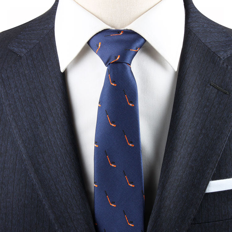 Close-up of a person wearing a pinstripe navy suit and white dress shirt with a Field Hockey Skinny Tie featuring an orange pattern, subtly incorporating field hockey motifs that evoke an athletic spirit.