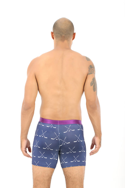 A shirtless person stands facing away, exuding a sense of coziness while wearing Crossed Ice Hockey Underwear, featuring a blue pattern and a pink waistband.