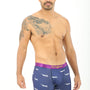 A man with a tattoo on his shoulder is modeling the relaxed style of Airplane Underwear, featuring cozy purple boxer briefs adorned with a pink waistband and shark pattern.