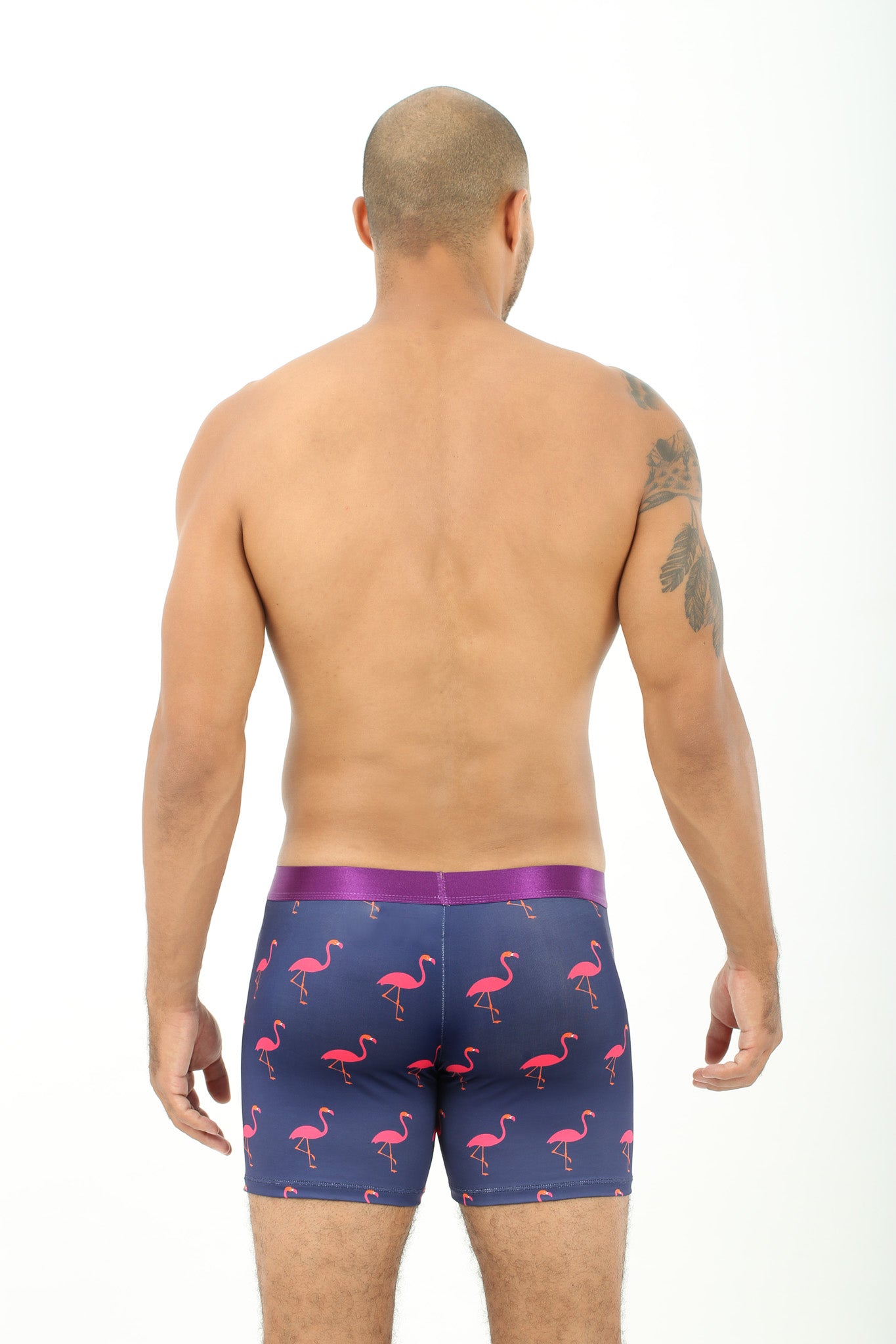 A man viewed from behind, wearing Pink Flamingo Underwear, showing a tattoo on his left shoulder as he strides forward with tropical vibes.