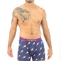 A man with a tattoo on his left arm is modeling Rocket Underwear, featuring blue boxer briefs adorned with rocket ship patterns for a delightful blend of comfort and cosmos-themed style.