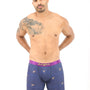 A man with a tattoo on his left shoulder poses wearing Goat Underwear blue boxer briefs with a purple waistband and small designs, epitomizing peak snugness against a plain white background.