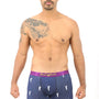 A man with a tattoo on his shoulder is modeling navy blue Golf Swing Underwear, featuring a purple waistband with "Two Cocks" written in cursive. Designed for ultimate comfort, the boxer briefs boast a pattern of small white rooster logos. Pair them with your favorite tee for an effortlessly stylish look.