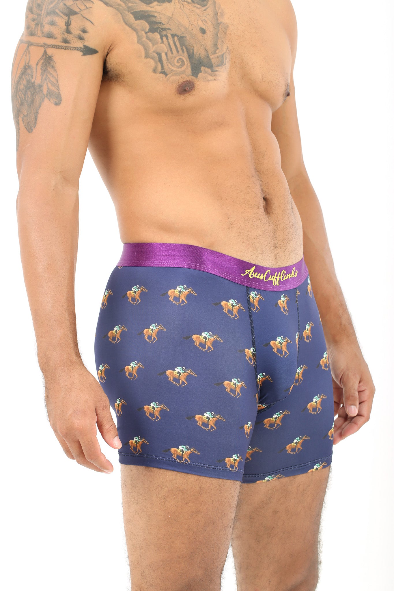 A person wearing Racing Horse Underwear in purple, featuring a playful pattern of grazing camels, stands against a plain white background.