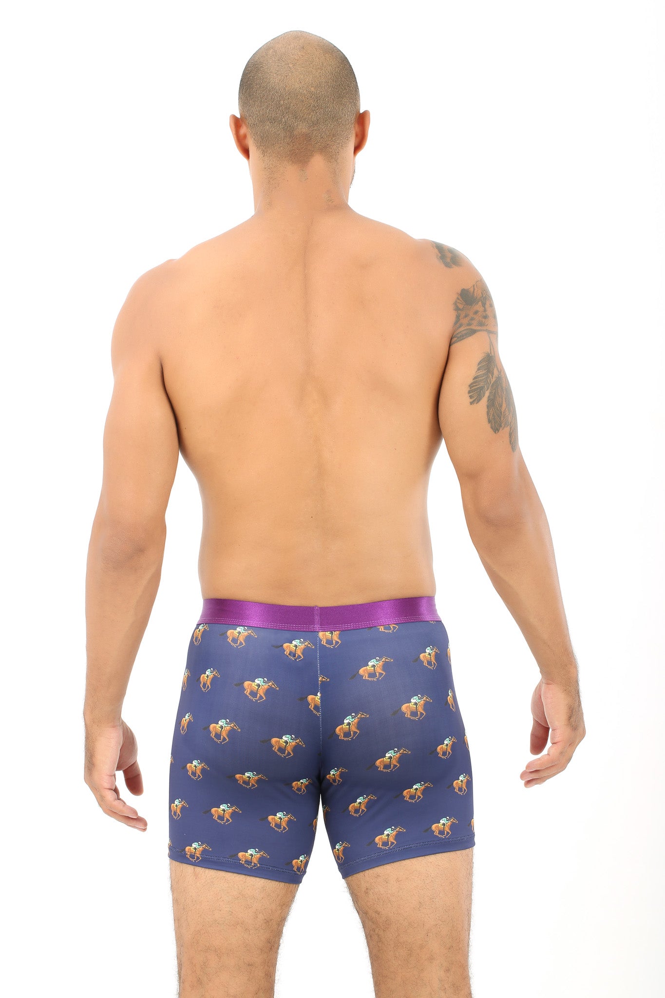 A man stands with his back to the camera, wearing Racing Horse Underwear in blue with a floral pattern and a purple waistband that hugs him like the gentle embrace of pastures.