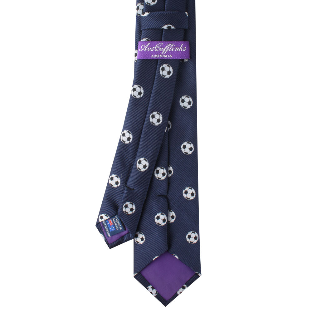 A navy blue tie with a pattern of soccer balls, exuding timeless class, features a purple label that reads "Soccer Skinny Tie.