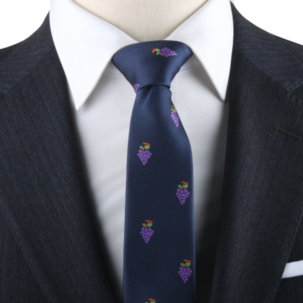 Close-up of a person wearing a dark suit and white shirt, complemented by the Grapes Skinny Tie, showcasing navy fabric adorned with small purple grape motifs, exuding a hint of vineyard sophistication.