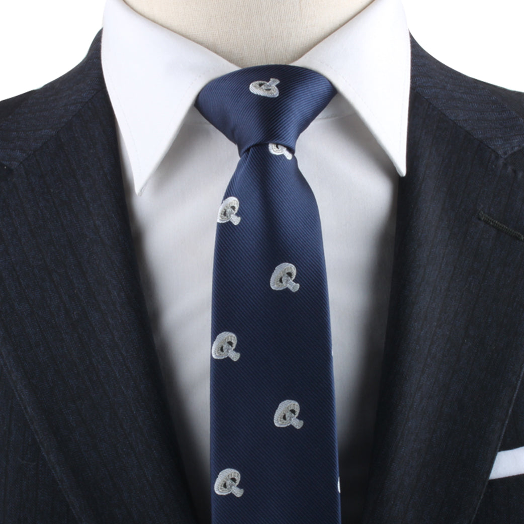 Close-up of a person wearing a dark pinstripe suit, white dress shirt, and the Mushrooms Skinny Tie—navy blue with elegant white embroidered lowercase 'q' patterns—exuding nature-inspired sophistication.