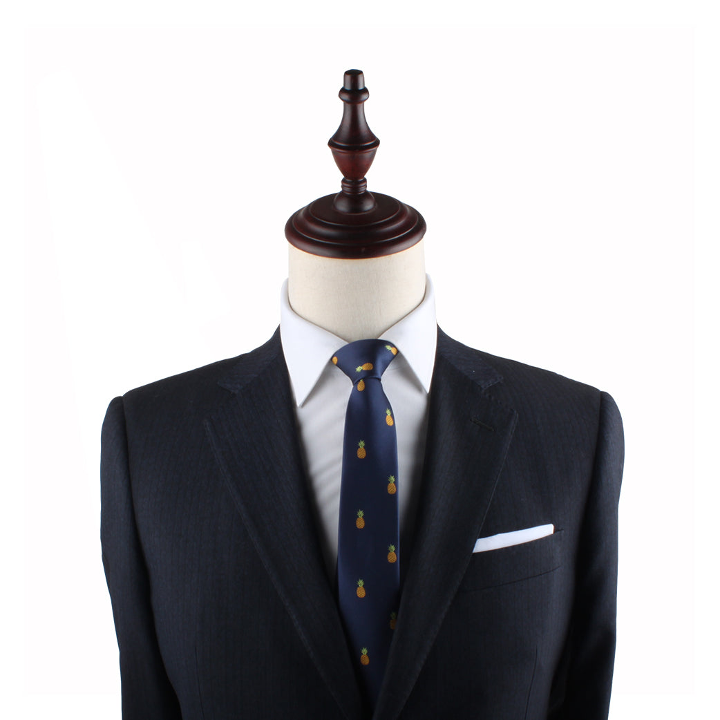 A dark blue pinstripe suit, white dress shirt, Pineapple Skinny Tie, and a white pocket square displayed on a mannequin with a wooden top exude modern elegance.