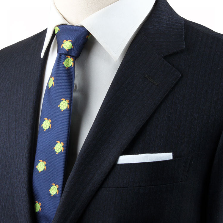 Close-up of a man wearing a navy blue suit and a Green Turtle Skinny Tie adorned with yellow flower patterns, exuding natural elegance with a white pocket square.