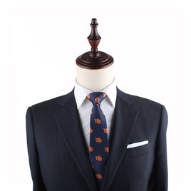 A suit on a tailor's mannequin, featuring a navy blue Pretzel Skinny Tie with an orange floral twist, paired with a white dress shirt and a dark blazer adorned with a white pocket square.