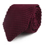 A rolled-up Maroon Knitted Skinny Tie with a textured pattern radiates cozy elegance against a white background.