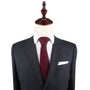 A mannequin dressed in a dark grey suit paired with a white shirt, a Maroon Knitted Skinny Tie, and a white pocket square exudes cozy elegance with its blend of warm hues.