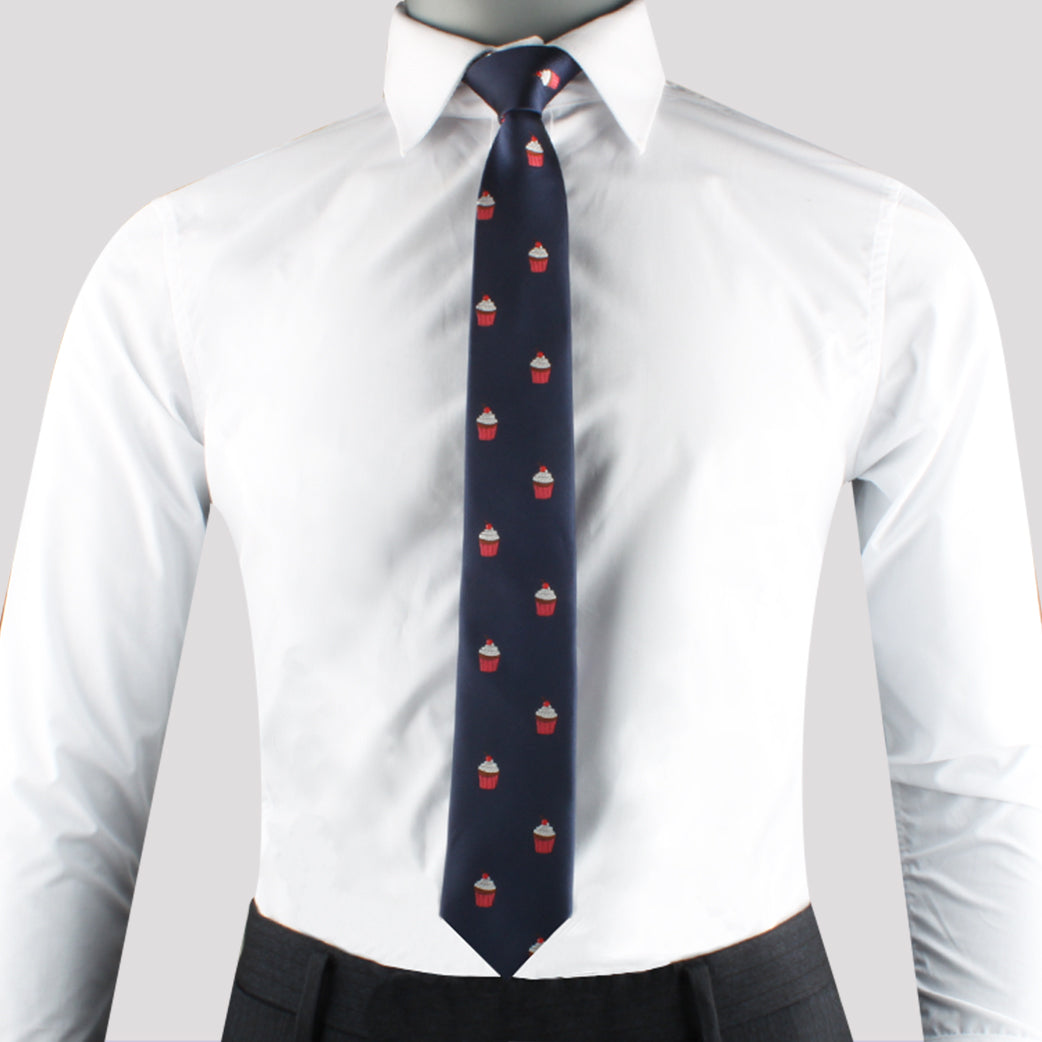 A person wearing a white dress shirt has made a delectable style statement with the Muffin Skinny Tie, featuring small red and white cupcake designs against a navy background.