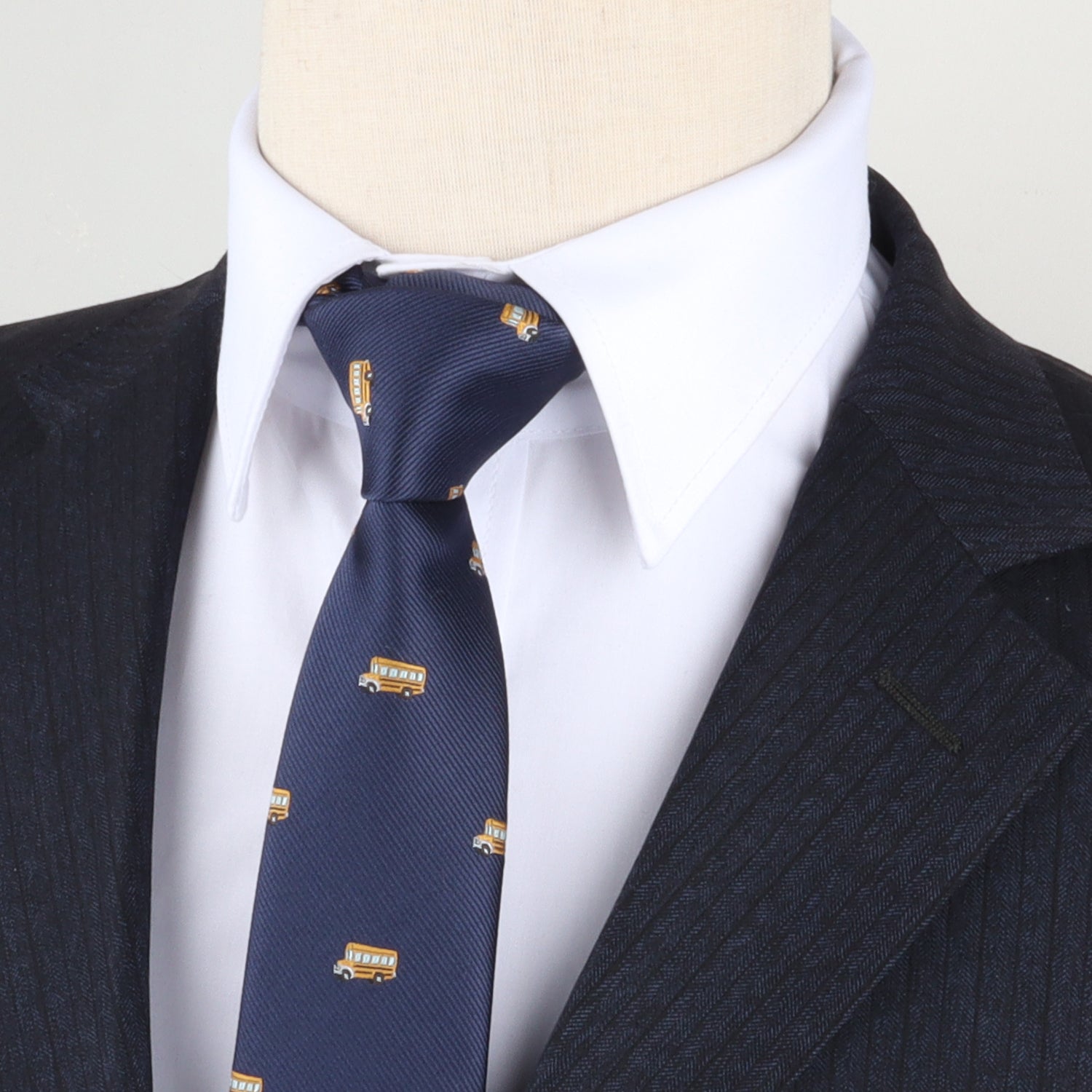 Close-up of a mannequin dressed in a pinstriped suit and white shirt, featuring a School Bus Skinny Tie with small emblem patterns.