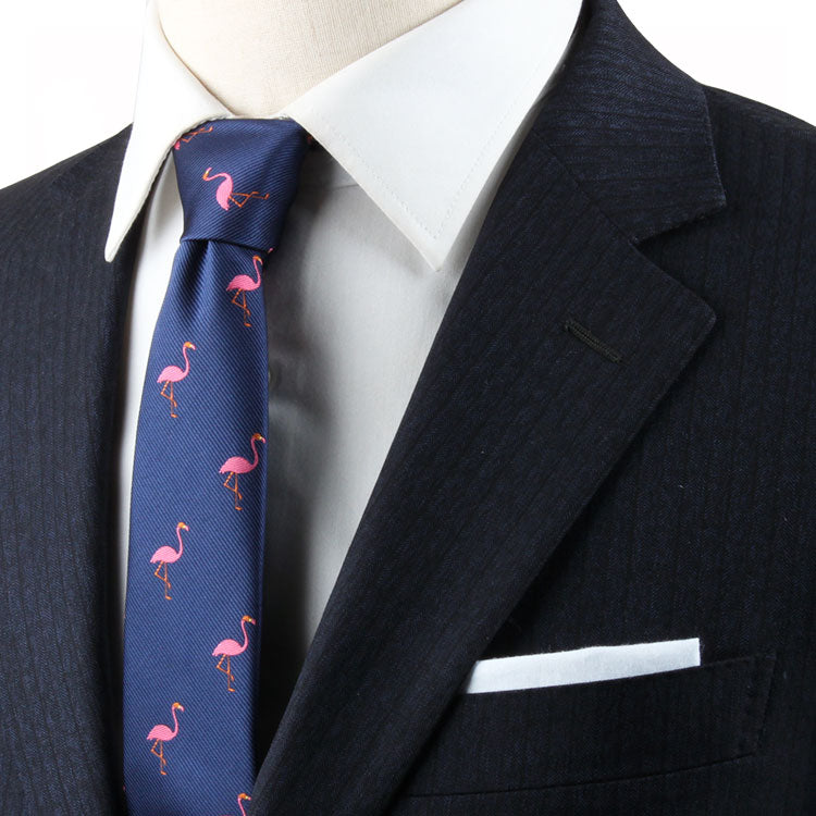 A person in a dark suit with a white shirt and the Flamingo Skinny Tie, featuring a whimsical flamingo pattern.