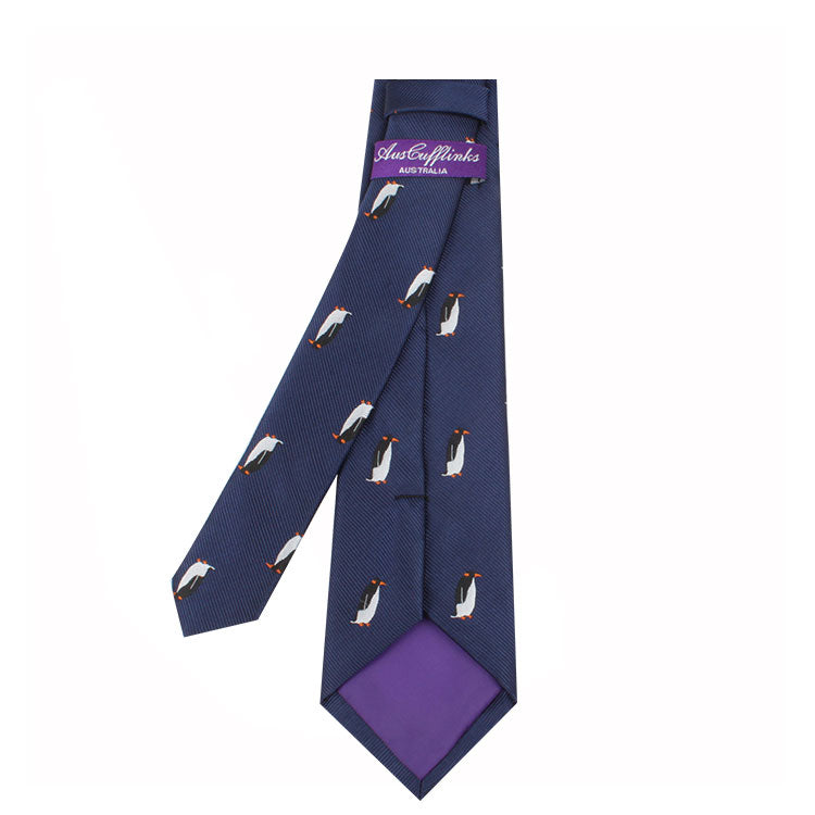 A Penguin Skinny Tie adorned with a whimsical charm of penguin patterns and a purple label that reads "Josh & Phinks Boutique" on the inner side.