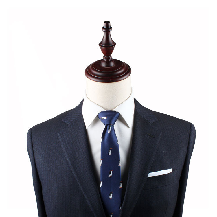 A dark blue pinstripe suit with a white dress shirt and a Penguin Skinny Tie is displayed on a mannequin, exuding timeless elegance.