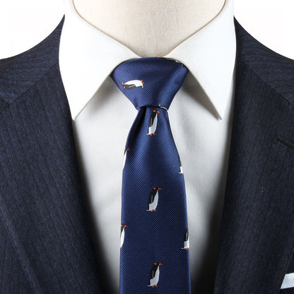 Close-up of a person wearing a dark blue suit and white dress shirt, featuring a Penguin Skinny Tie with small penguin designs that add whimsical charm.