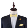 A mannequin dressed in a dark suit with a crisp white shirt highlights the vibrancy of the Baby Yellow Bow Tie, perfectly complemented by a matching pocket square and flower lapel pin.