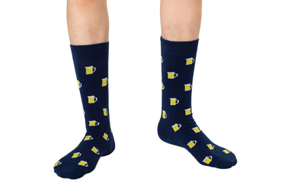 A person stands on a white background wearing Beer Socks in navy blue, featuring yellow beer mug patterns—perfect for beer lovers.