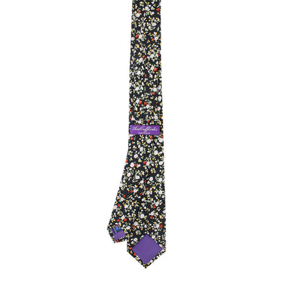 The Multi Floral Skinny Cotton Tie radiates pastel sophistication with its floral pattern and black base, featuring a purple label that reads "Made in America" and matching purple lining at the tips to enhance its business finesse.