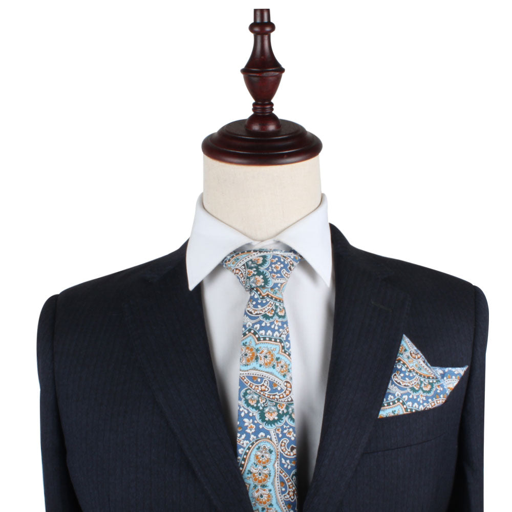 A mannequin elegantly dressed in a dark suit exudes sophistication with a blue and orange paisley tie, complemented by the Blue Paisley Pocket Square, meticulously folded to perfection.