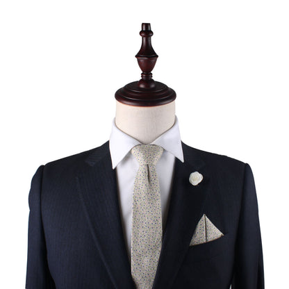 A dark suit exudes elegance, enhanced by the Blue Forget-Me-Nots Cotton Floral Skinny Tie & Pocket Square Set, with its light pattern and subtle blue accents, tastefully displayed on a mannequin with a wooden stand.