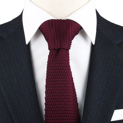 A close-up of a person wearing a dark pinstripe suit, a white dress shirt, and the Maroon Knitted Skinny Tie, exuding cozy elegance with the warm hues of the ensemble.
