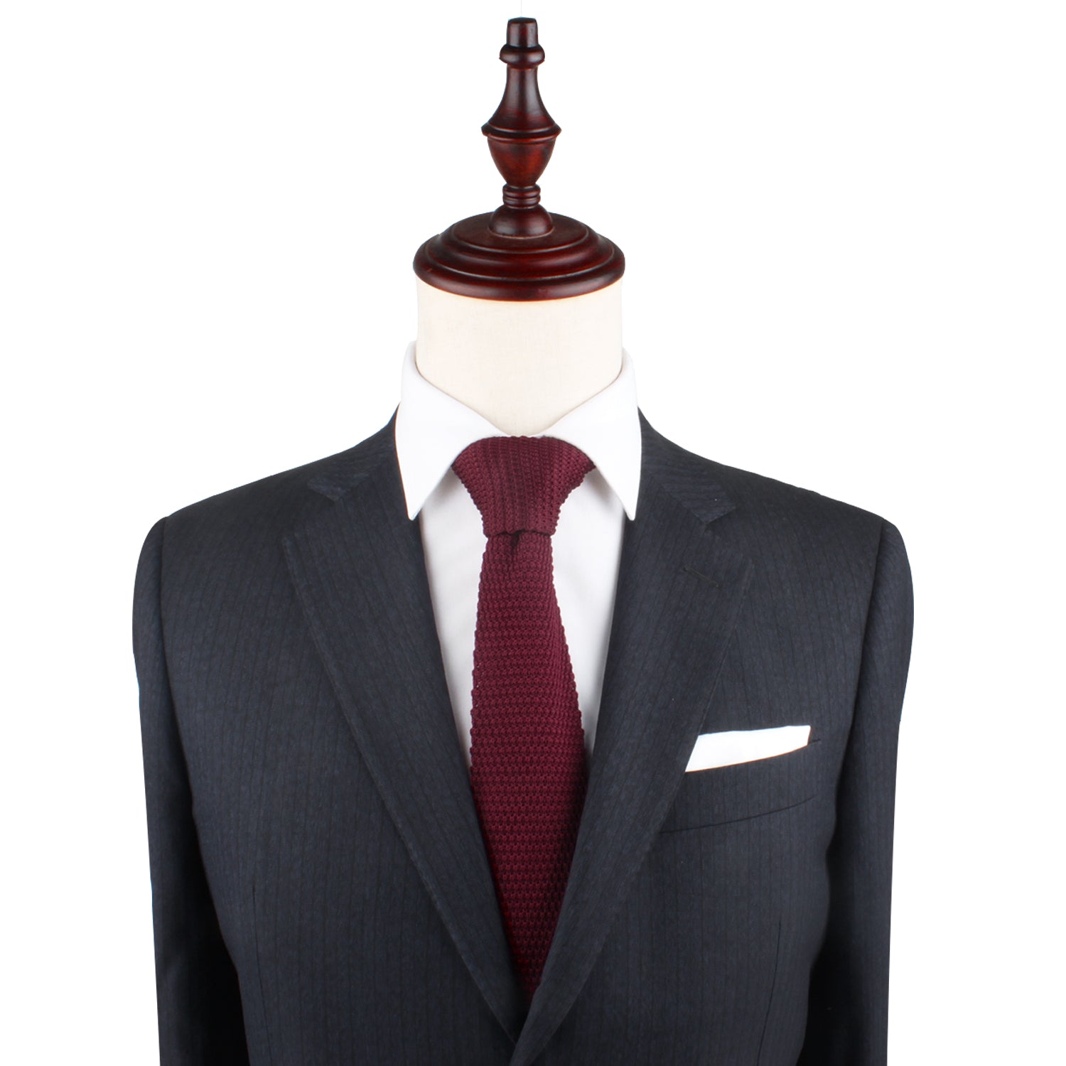 A mannequin dressed in a dark grey suit paired with a white shirt, a Burgundy Knit Tie, and a white pocket square exudes cozy elegance with its blend of warm hues.