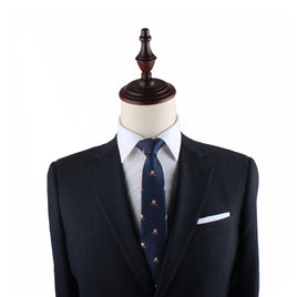 A tailored black suit on a mannequin exudes elegance, complemented by a white shirt and the Cake Slim Tie with a blue pattern against a plain white background.
