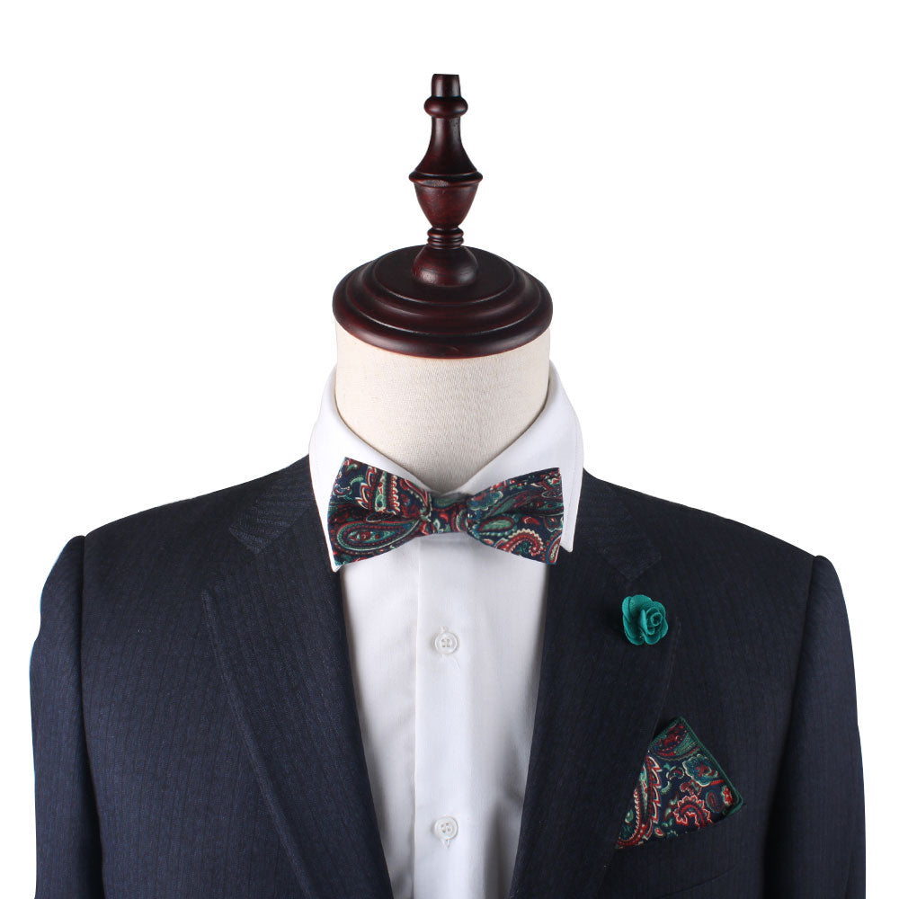 A mannequin in a dark suit and white shirt exudes sophistication with a paisley bow tie, green floral lapel pin, and the Carpe diem Paisley Pocket Square. This elegant ensemble is ideal for weddings, displayed on a crisp white background.