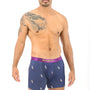 A man with a shaved head and tattoos on his arm is wearing Cat Boxer, navy blue boxer briefs featuring a purple waistband, embodying the snugness reminiscent of a cat's nine lives.