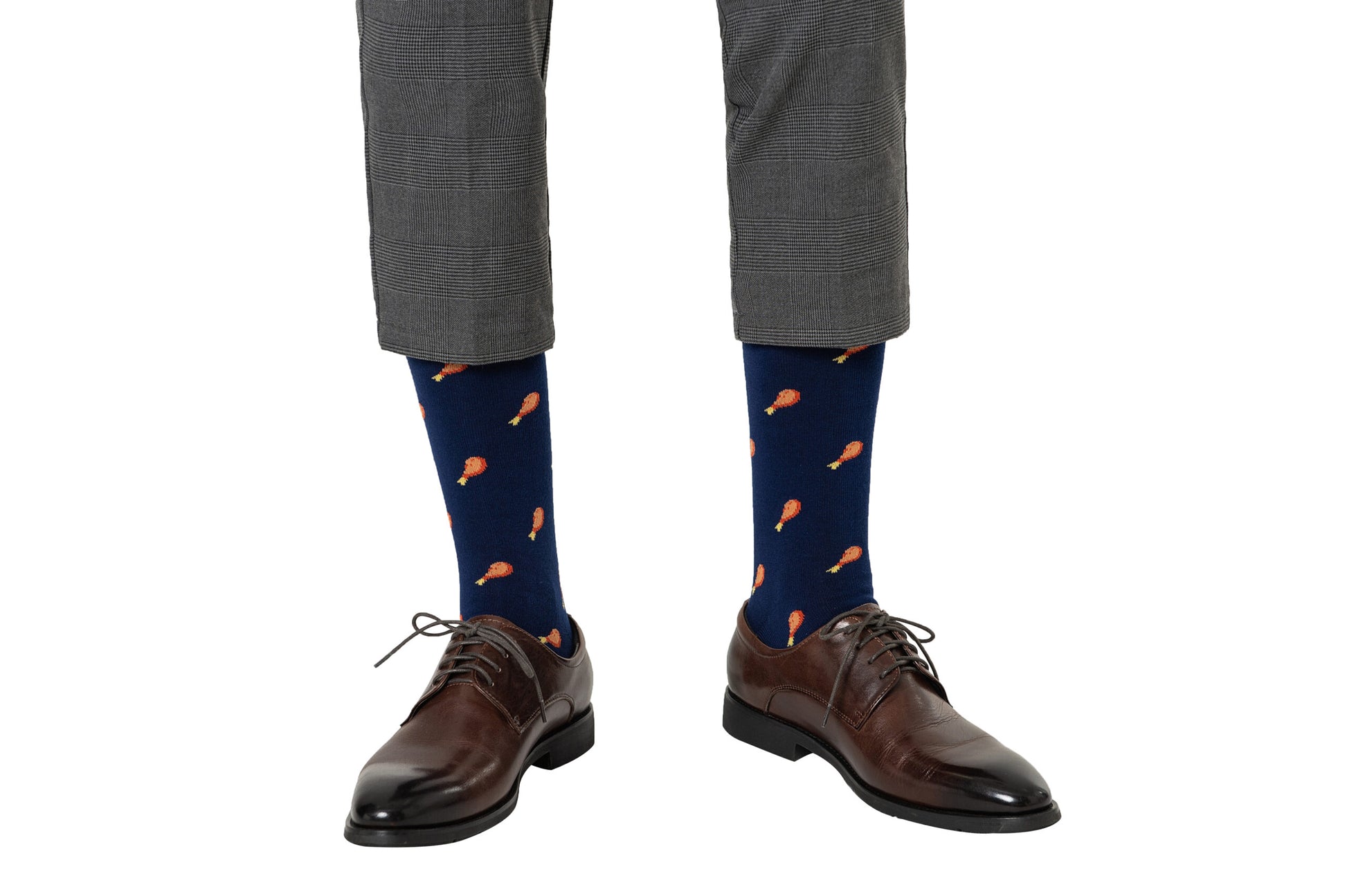 A person exhibiting a layered style is wearing gray plaid pants, brown dress shoes, and orange-patterned Strawberry Cake Socks.