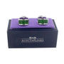 A pair of Emerald Green Cufflinks rests on a purple cushion, elegantly placed in a black box labeled "AUSCUFFLINKS," exuding a touch of regal sophistication.