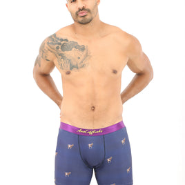 A man with a tattoo on his left shoulder poses wearing Goat Boxers blue boxer briefs with a purple waistband and small designs, epitomizing peak snugness against a plain white background.