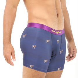 A man stands confidently, showcasing his Goat Underwear blue boxer briefs adorned with dog prints and a striking purple waistband. Visible tattoos decorate his torso, adding to the aura of mountainous comfort he exudes.