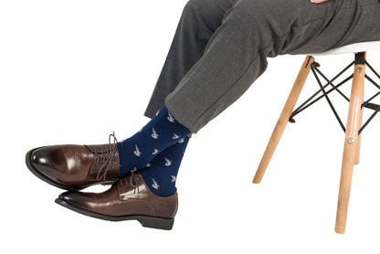 Person wearing brown leather shoes, Shark Socks that add a splash of deep-sea style with their bird patterns, and grey plaid trousers, seated on a white chair with wooden legs.
