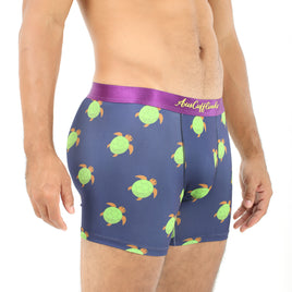 A person relishing the leisurely comfort of Green Turtle Underwear, featuring a blue hue with a charming turtle pattern and complemented by a purple waistband.