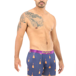A man with a tattooed arm stands against a white background, wearing Guitar Boxer in blue, which captures the relaxed vibe of strumming chords.