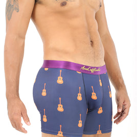 A man stands against a white background, mimicking guitar playing while wearing Guitar Underwear, which features a guitar pattern on blue boxer briefs with a purple waistband, effortlessly combining style and comfort.