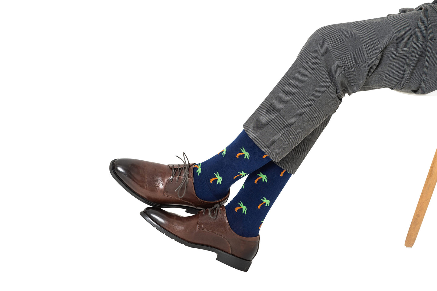 Person wearing gray pants, brown dress shoes, and the Hawaiian Socks, seated with legs crossed, exuding tropical vibes.