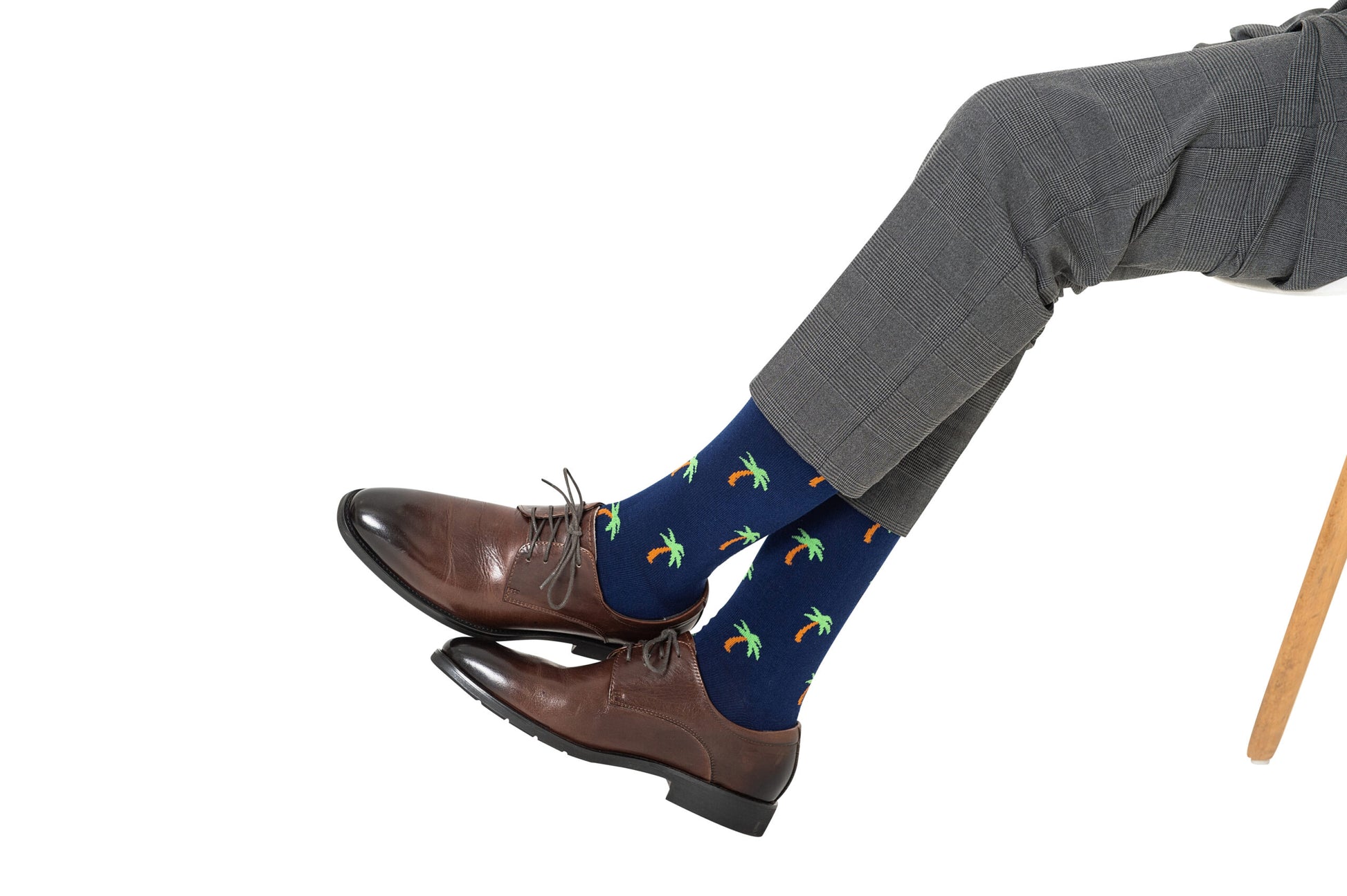 Person wearing gray pants, brown dress shoes, and the Hawaiian Socks, seated with legs crossed, exuding tropical vibes.