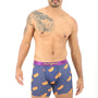 A man stands confidently, showcasing a distinctive style in his Hotdog Boxer—purple boxers decorated with hot dog prints. The tattoo on his left shoulder and arm enhances his appearance, seamlessly combining comfort with personal flair.
