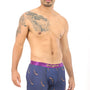 A man stands wearing the Ice Hockey Boxer, showcasing patterned navy boxer briefs with a purple waistband and "AndCliffCrub" lettering. He embodies a relaxed vibe, effortlessly combining comfort and style, with a tattoo on his left shoulder and chest.
