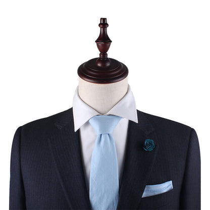 Mannequin dressed in a dark suit with a white dress shirt, Light Blue Skinny Cotton Tie, pocket square, and a rose-shaped pin on the left lapel.