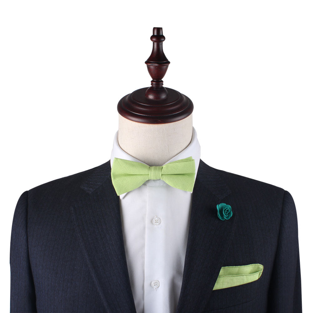 A mannequin dons a black suit with a white shirt, complemented by a vibrant green bow tie, the Lime Green Cotton Pocket Square, and a bold green floral lapel pin.