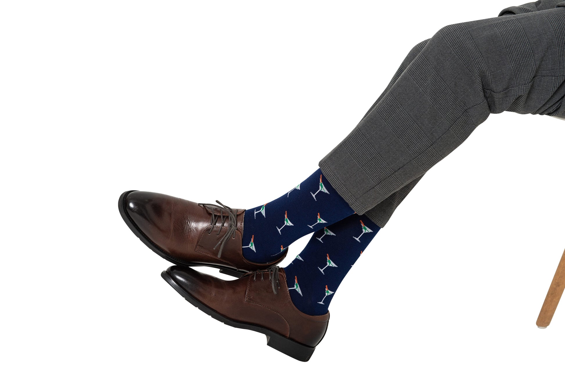 A person elevates their sock game with the Martini Margarita Socks, which boast a colorful kite pattern on a blue background, perfectly contrasting the classic look of dark brown dress shoes and gray pants.