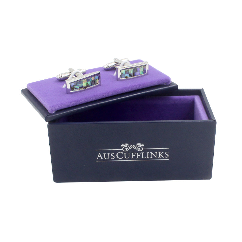 A pair of Mother of Pearl Stone Cufflinks, capturing the ocean's depths, rest on a purple velvet display in an open black box labeled "AUSCUFFLINKS.